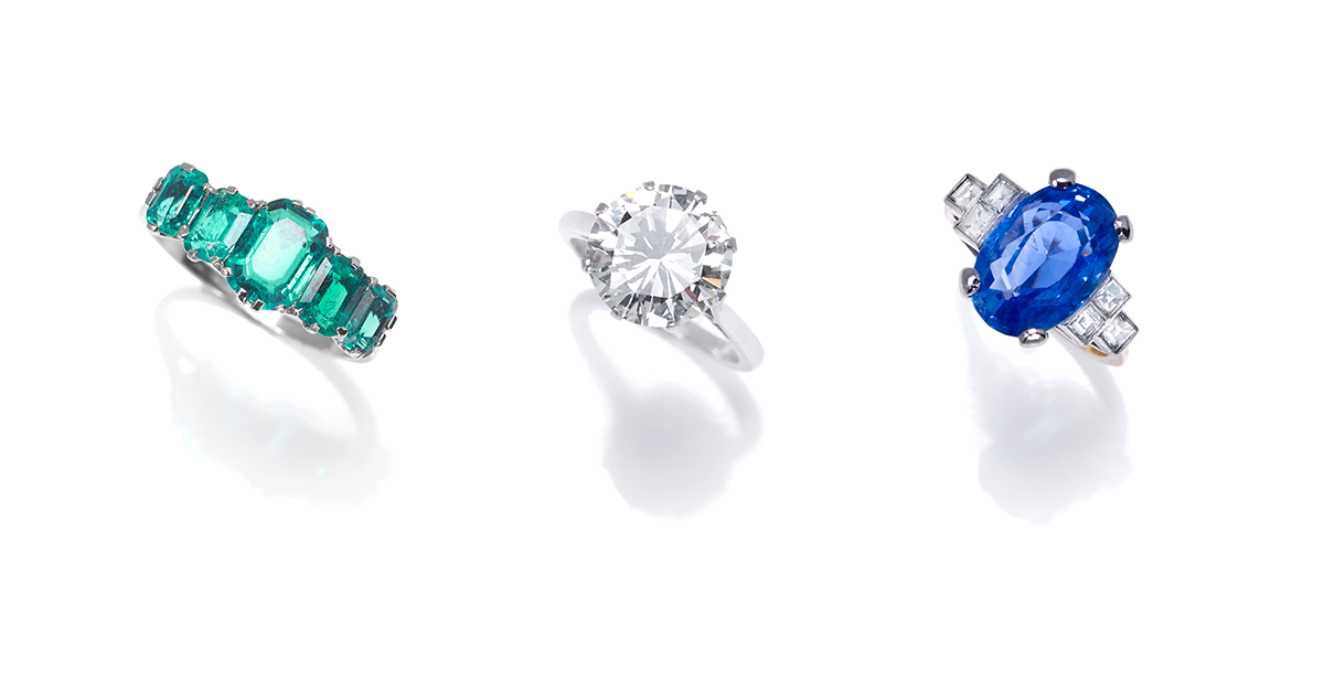 Three engagement rings: five stone emerald ring, single-stone diamond ring, sapphire and diamond ring. 